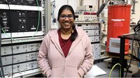 Lakshmi Bhaskaran im Rechenzentrum, stehend in rosa Jacke vor technischen Geräten.